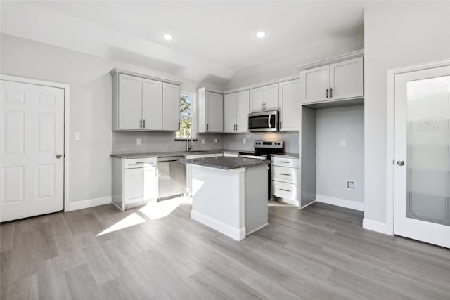 kitchen with sink, a center island, dark stone counters, light hardwood / wood-style floors, and appliances with stainless steel finishes