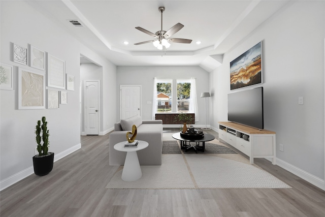 living room featuring ceiling fan, light wood-type flooring, and a tray ceiling