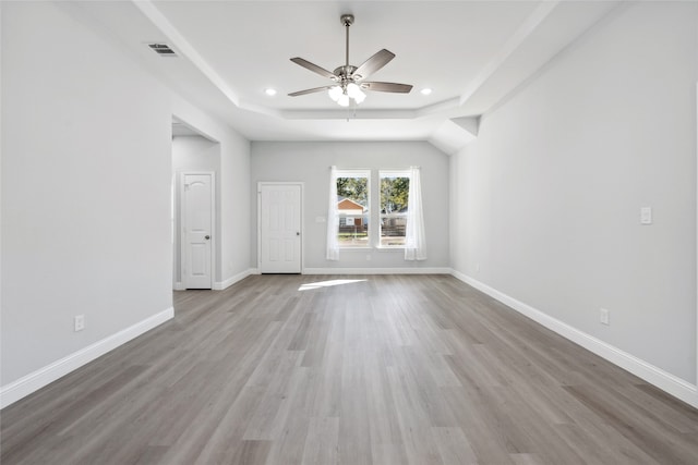 unfurnished room with a raised ceiling, ceiling fan, and light wood-type flooring