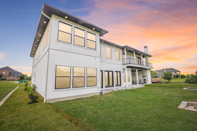 back house at dusk featuring a yard, a balcony, and a patio