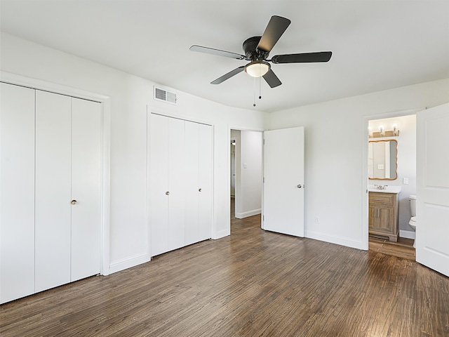 unfurnished bedroom featuring dark hardwood / wood-style flooring, ensuite bathroom, ceiling fan, and multiple closets