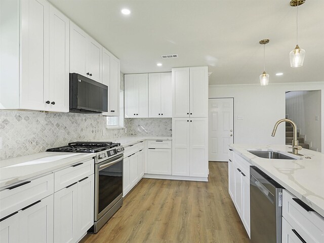 kitchen with white cabinets, appliances with stainless steel finishes, light stone counters, and pendant lighting