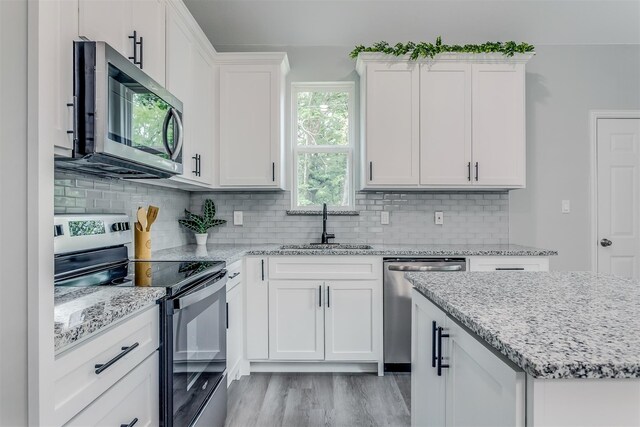 kitchen featuring light wood-type flooring, tasteful backsplash, stainless steel appliances, sink, and white cabinets