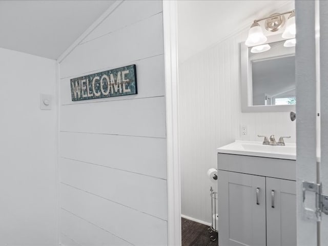 bathroom featuring hardwood / wood-style flooring, vanity, wooden walls, and vaulted ceiling