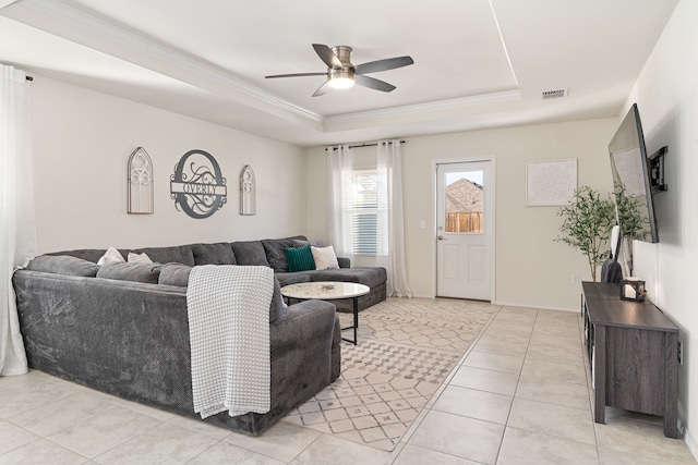 living room with a tray ceiling, ceiling fan, light tile patterned flooring, and ornamental molding