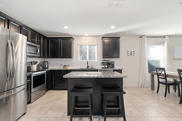 kitchen with sink, light stone counters, backsplash, a kitchen island, and appliances with stainless steel finishes