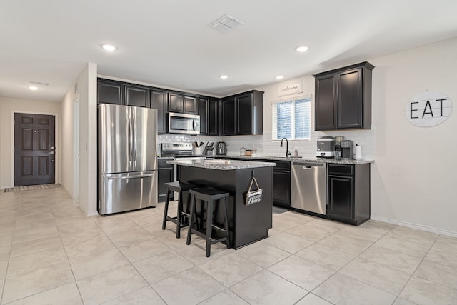 kitchen with a center island, sink, appliances with stainless steel finishes, light stone counters, and a breakfast bar area