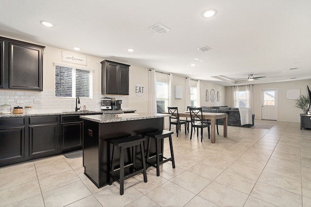 kitchen featuring ceiling fan, sink, light stone countertops, light tile patterned floors, and a kitchen island