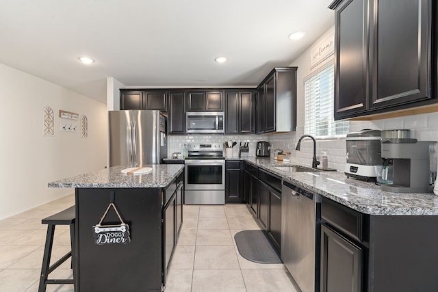 kitchen featuring light stone countertops, appliances with stainless steel finishes, decorative backsplash, a kitchen bar, and a center island