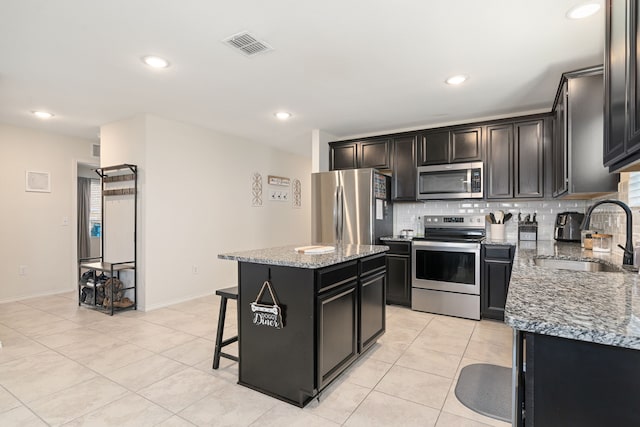 kitchen with light tile patterned flooring, sink, appliances with stainless steel finishes, a kitchen island, and light stone counters