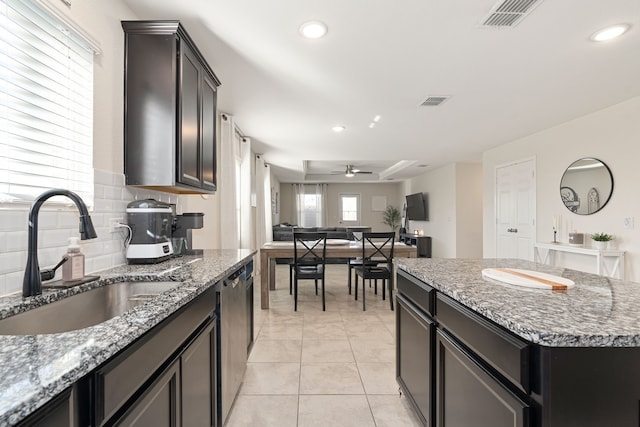 kitchen with a center island, backsplash, sink, ceiling fan, and light stone counters