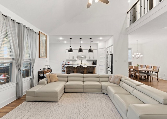 living room with ceiling fan with notable chandelier, light hardwood / wood-style flooring, and high vaulted ceiling