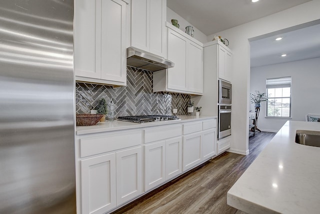 kitchen featuring white cabinetry, stainless steel appliances, wood-type flooring, decorative backsplash, and exhaust hood