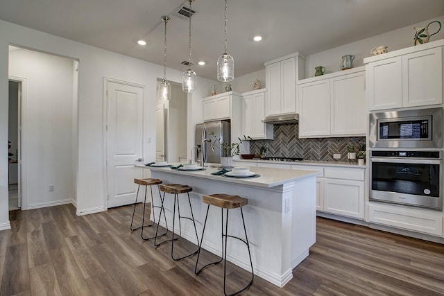 kitchen featuring pendant lighting, backsplash, a kitchen island with sink, appliances with stainless steel finishes, and white cabinetry