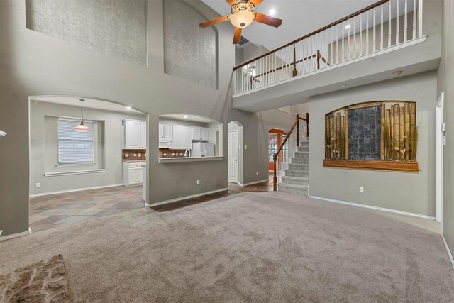 unfurnished living room with carpet flooring, ceiling fan, and a high ceiling