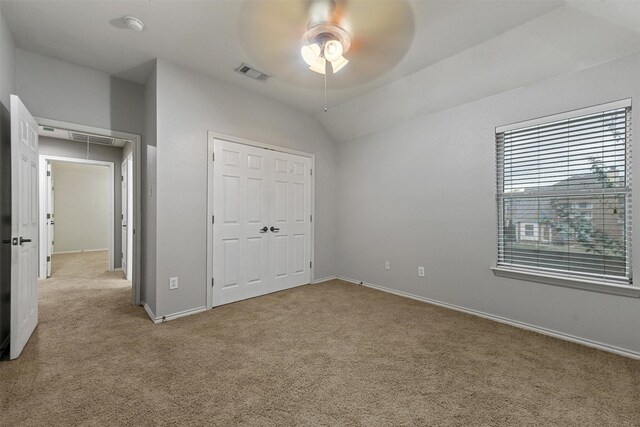 unfurnished bedroom with light colored carpet, a closet, lofted ceiling, and ceiling fan