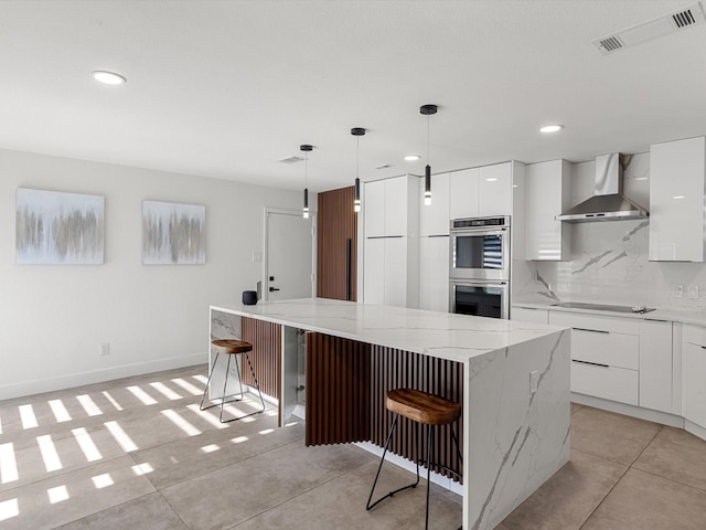 kitchen featuring white cabinetry, wall chimney exhaust hood, stainless steel double oven, a kitchen breakfast bar, and a kitchen island