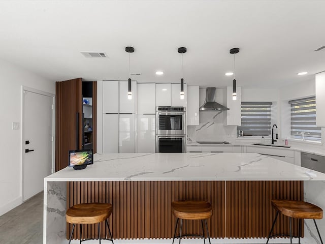 kitchen featuring a kitchen bar, pendant lighting, wall chimney exhaust hood, and sink