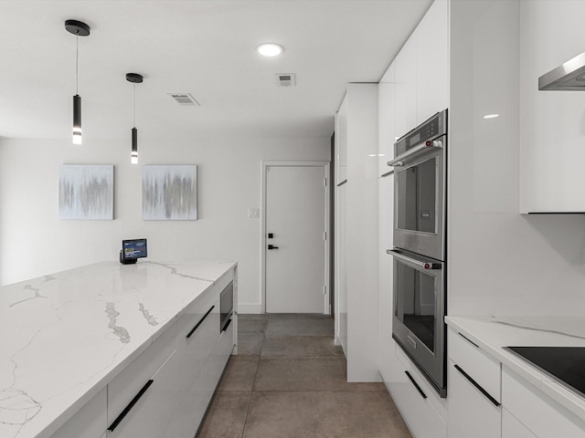 kitchen with light stone counters, stainless steel double oven, built in microwave, pendant lighting, and white cabinetry