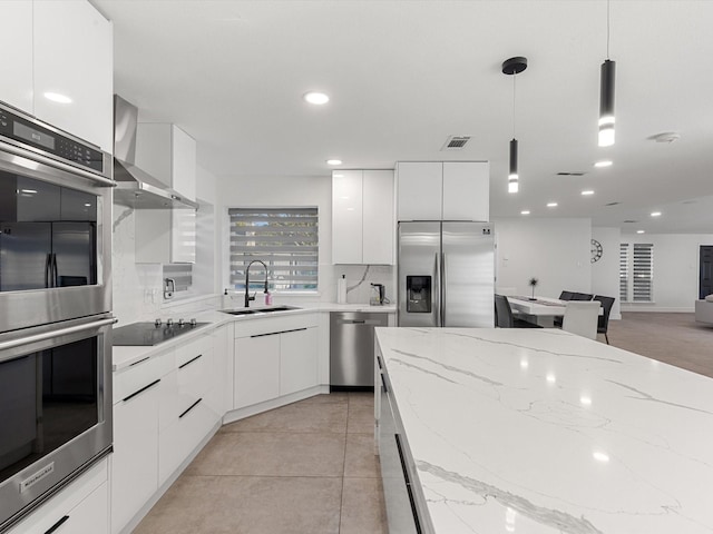 kitchen with appliances with stainless steel finishes, wall chimney range hood, sink, white cabinetry, and hanging light fixtures