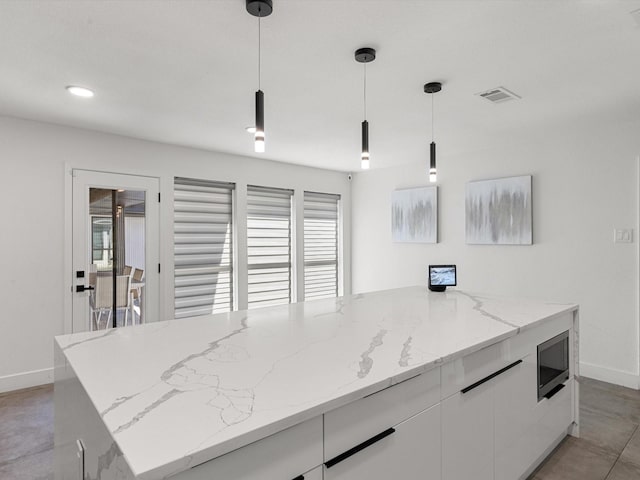 kitchen with white cabinets, decorative light fixtures, a kitchen island, and stainless steel microwave