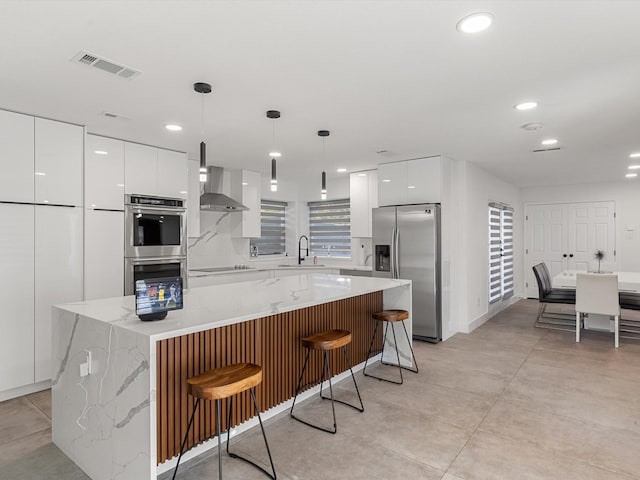 kitchen with a kitchen bar, wall chimney exhaust hood, stainless steel appliances, a kitchen island, and hanging light fixtures