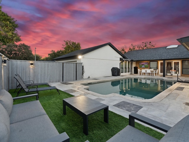 pool at dusk featuring a lawn and a patio