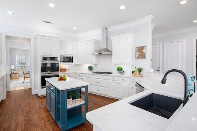 kitchen featuring sink, wall chimney exhaust hood, a kitchen island, white cabinets, and appliances with stainless steel finishes