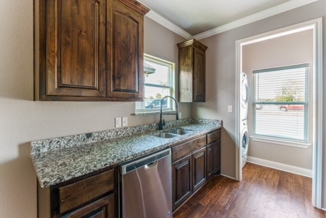 kitchen featuring dishwasher, a wealth of natural light, dark hardwood / wood-style flooring, and stacked washer / drying machine