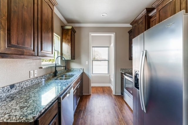 kitchen with light stone counters, stainless steel appliances, crown molding, dark wood-type flooring, and sink