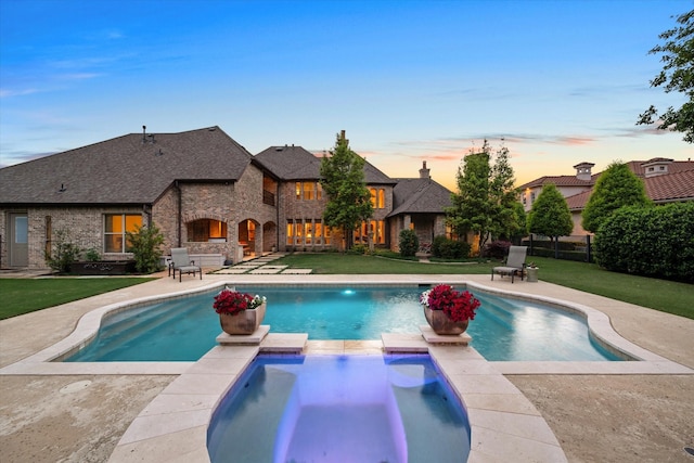 pool at dusk featuring a lawn, an in ground hot tub, and a patio