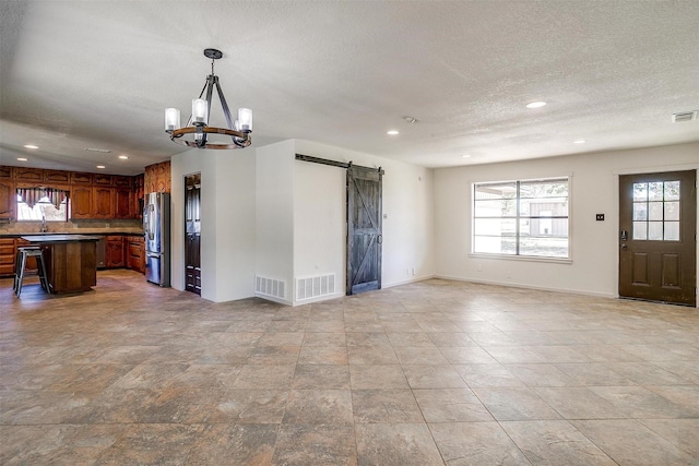 interior space with a barn door, a breakfast bar area, hanging light fixtures, stainless steel refrigerator, and a chandelier