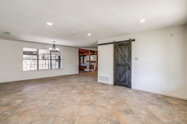 unfurnished room featuring a textured ceiling, an inviting chandelier, and a barn door