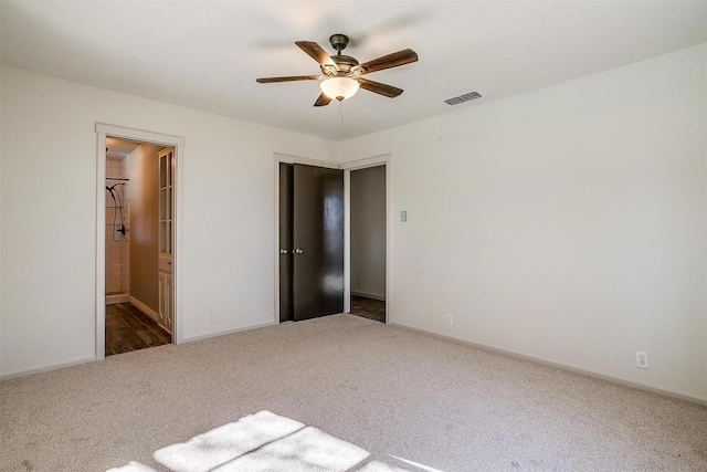 unfurnished bedroom with ceiling fan, dark carpet, and ensuite bathroom