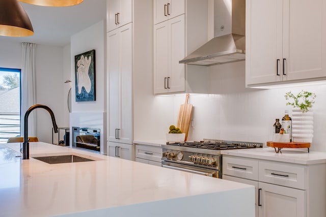 kitchen with white cabinets, wall chimney range hood, sink, and high end stainless steel range