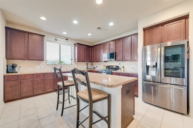 kitchen with light tile patterned flooring, a breakfast bar area, light stone countertops, a kitchen island, and stainless steel appliances