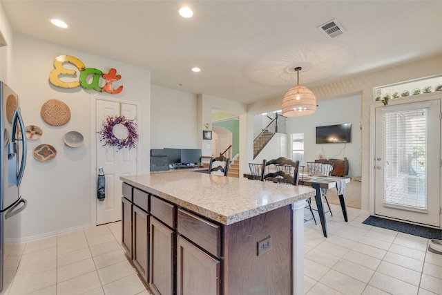 kitchen featuring stainless steel refrigerator, a center island, hanging light fixtures, dark brown cabinets, and light tile patterned floors