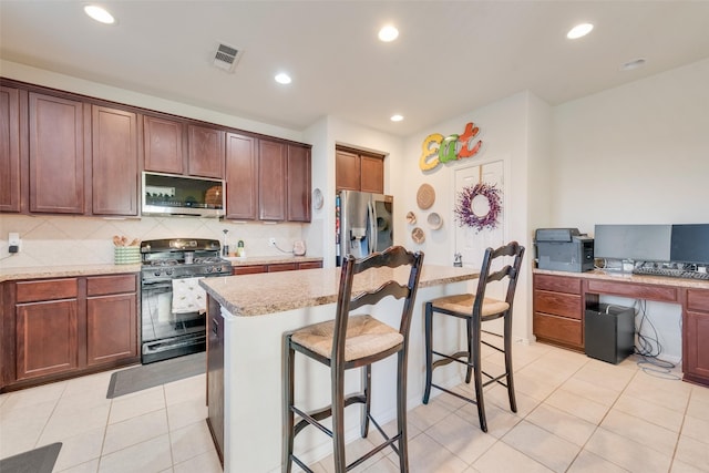 kitchen featuring appliances with stainless steel finishes, a kitchen breakfast bar, tasteful backsplash, light tile patterned floors, and a kitchen island