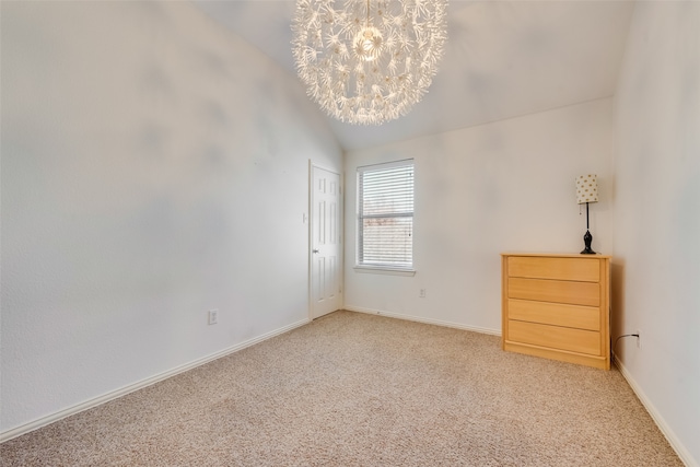 carpeted spare room featuring a notable chandelier and vaulted ceiling