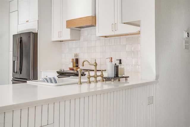 kitchen featuring white cabinets, decorative backsplash, stainless steel fridge, and custom range hood