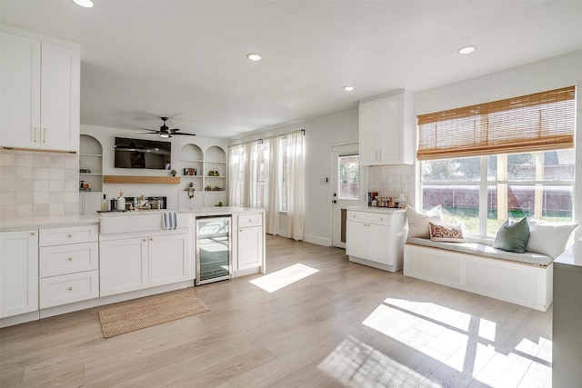 kitchen with white cabinets, light wood-type flooring, backsplash, and wine cooler