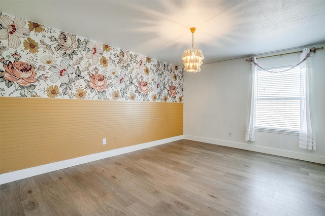 empty room with hardwood / wood-style flooring, wood walls, a textured ceiling, and a chandelier