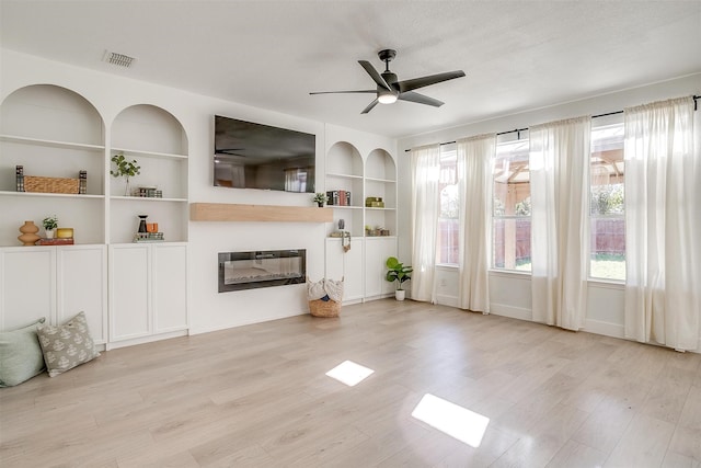 unfurnished living room featuring ceiling fan, light hardwood / wood-style floors, built in features, and a textured ceiling