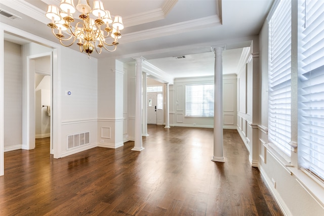 interior space featuring decorative columns, ornamental molding, a raised ceiling, dark wood-type flooring, and a notable chandelier