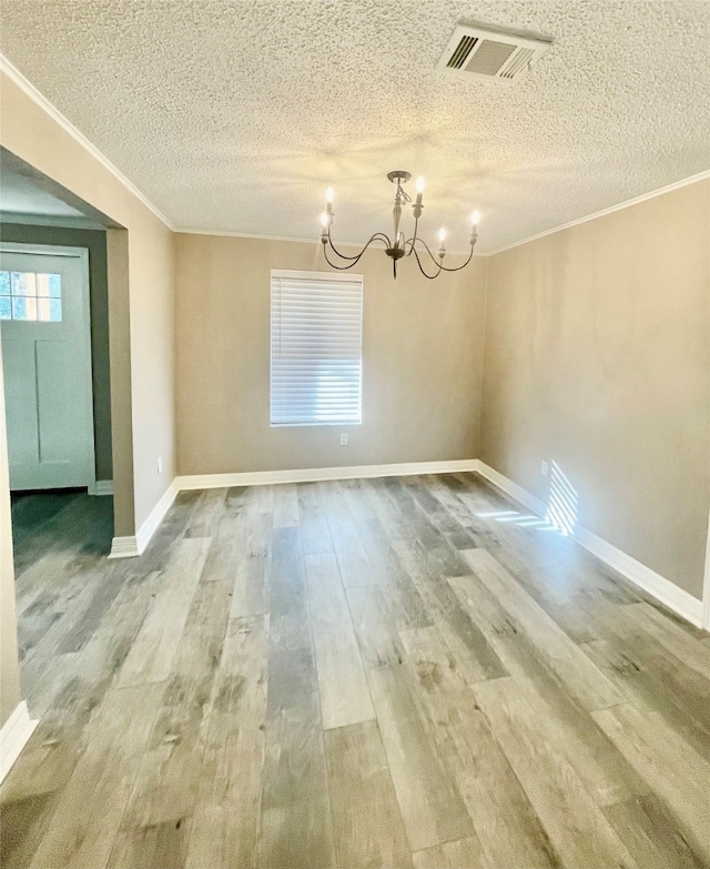 unfurnished dining area with a textured ceiling, wood-type flooring, ornamental molding, and a chandelier