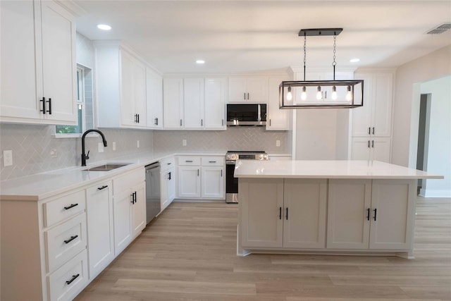 kitchen featuring pendant lighting, white cabinets, sink, a kitchen island, and stainless steel appliances