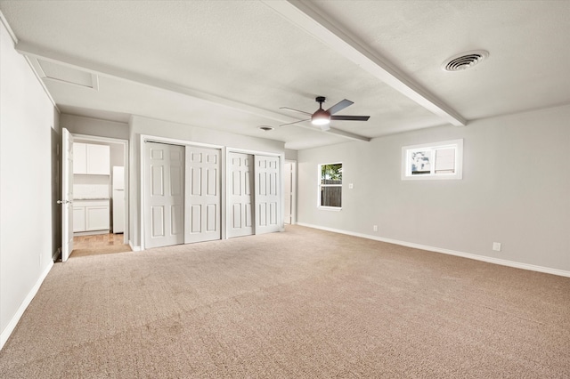 unfurnished bedroom with light carpet, beam ceiling, ceiling fan, and multiple closets