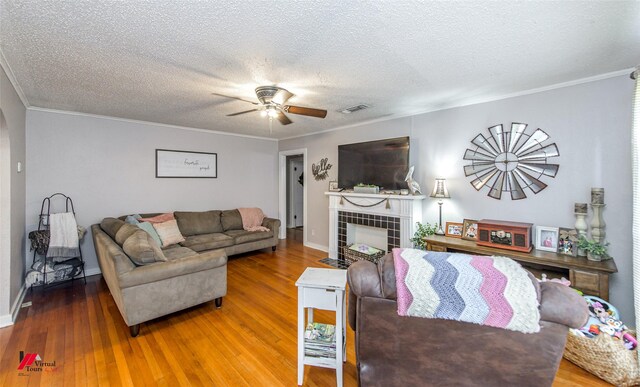 living room featuring wood-type flooring, crown molding, and a tiled fireplace