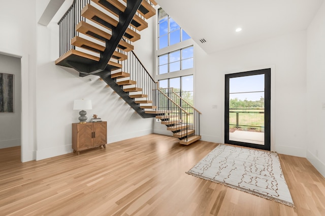 foyer entrance with a towering ceiling, a wealth of natural light, and light hardwood / wood-style flooring