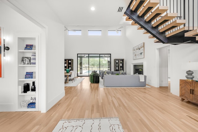 unfurnished living room featuring a towering ceiling, light hardwood / wood-style floors, and built in features